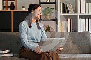 Nice asian woman using laptop computer on couch and smiling moment.