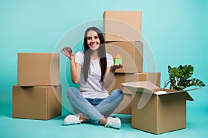 Nice attractive cheery girl sitting in lotus pose with pile stack boxes holding in hands house figure keys realestate