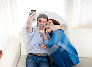 Nice attractive young couple sitting together in sofa couch taking selfie photo with mobile phone