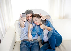 Nice attractive young couple sitting together in sofa couch taking selfie photo with mobile phone