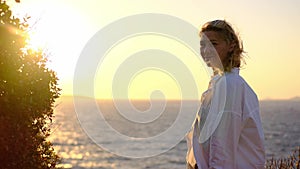 Nice attractive young woman at sunset on background of ocean or sea in white shirt and black top looks into distance