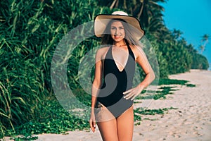 A nice beautiful girl came to the islands to rest, wears a trendy swimsuit, a beach hat, smiles and enjoys vacation.