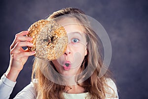 Blond girl looking through a big bagel