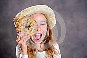 Blond girl with straw hat looking through a big bagel