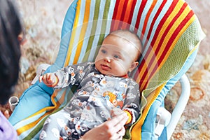 nice blue eyed Baby child relaxing on a sunbed or a deck chair colored bouncer at home