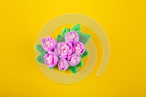 Nice bouquet made of modelling clay laying on yellow background. Top view, copy, space for text