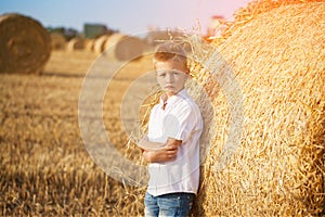 The nice boy in the field of near stack of straw at sunset