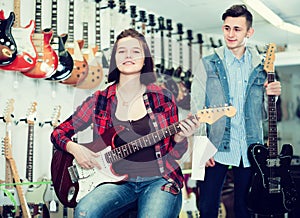 Nice boy and girl teenagers examining electric guitars