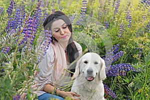 nice brunette girl posing with golden retriver at blooming Lupins meadow at country side. cloudy evening