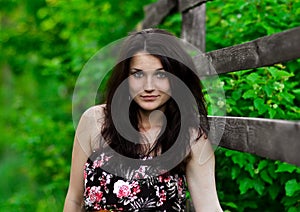 Nice brunette girl stand near the wooden fence, summer forest