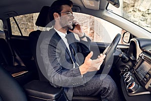 Nice business talk. Handsome young businessman talking on his smart phone and smiling while sitting on the front seat