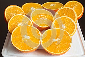 Nice composition of fresh oranges cut in half on a white cutting board on the dark kitchen table.