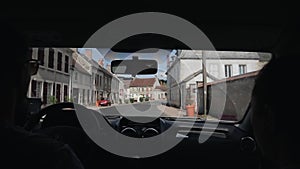 A nice couple goes by car along a narrow street lined with small houses