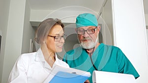 Nice couple, two doctors, a man and a woman, in medical gowns with folders in their hands, look into the frame and smile