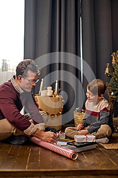 Nice dad drawing painting with adorable little kid son, sitting near Christmas tree