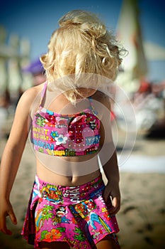 Nice dressed blond little girl on the beach in the summertime looking down