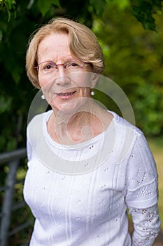 A nice elderly woman is smiling at the camera in a beautiful garden