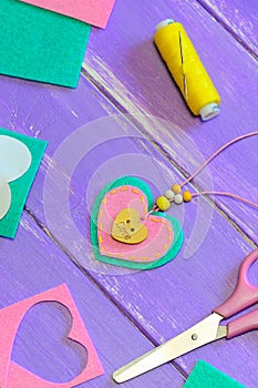 Nice felt heart pendant necklace. Scissors, thread, felt sheets and pieces on a purple wooden background. Valentines Day gift idea