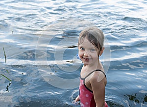 A nice four-year old girl stands smiling and laughing in the open water.