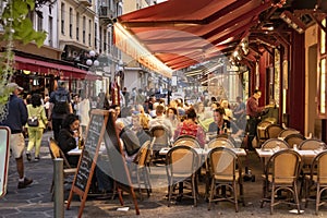 Guests in a restaurant with tables and chairs on the sidewalk at a street in Nice, France, in the dusk