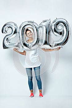 Nice funny girl dressed in white t-shirt, jeans and pink socks holding balloons in the shape of numbers 2019 on the