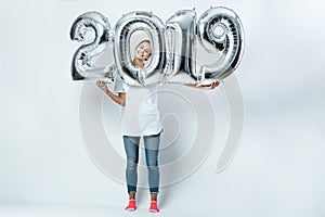 Nice funny girl dressed in white t-shirt, jeans and pink socks holding balloons in the shape of numbers 2019 on the