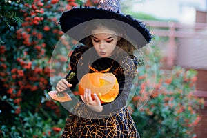 Nice girl of 8-9 years in suit for Halloween with a pumpkin into hands.