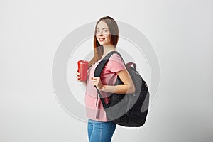 Nice girl with a black backpack on her shoulder dressed in a pink t-shirt and jeans holds a red plastic cup in her hand