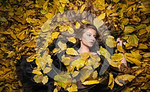 Nice girl covered with autumnal leaves. Young woman laying down on the ground covered by fall foliage in park. Beautiful girl