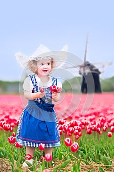 Nice girl in Dutch costume in tulips field with windmill