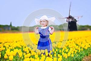 Nice girl in Dutch costume in tulips field with windmill