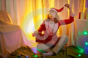 Nice girl in a red dress and hat of Santa with big red gift box in room decorated for Christmas. Woman in beautirul studio during