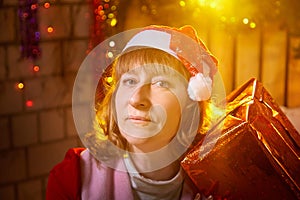 Nice girl in a red dress and hat of Santa with big red gift box in room decorated for Christmas. Woman in beautirul