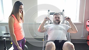 Nice girl trainer explains to a caucasian man the correctness of doing an exercise for leg muscles on a hackenshmidt