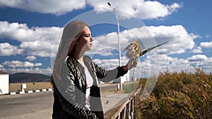 Nice girl or young woman in jacket sitting and blowing on reed flowers in her hand waiting for somebody. Slow motion