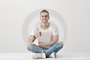 Nice idea to meet on fresh air. Portrait of handsome young male hacker in glasses sitting on floor with crossed legs