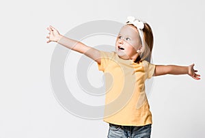 Nice kid baby girl in yellow t-shirt is singing with her hands up spread, playing, dancing