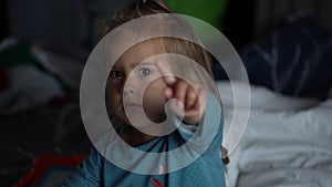 A nice little caucasian toddler baby is funny smiling, sitting on the bed at home. Portrait of a playful and energetic