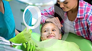 Nice little girl happy after dental procedures, admiring healthy teeth in mirror