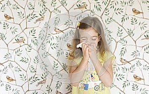A nice little girl sneezes into a handkerchief because she has a seasonal allergy to pollen and flowering plants. A sick child