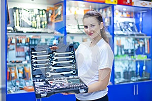 Nice looking girl saleswoman offers set of tools in an auto parts store. Ready to repair the car