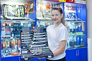 Nice looking girl saleswoman offers set of tools in an auto parts store. Ready to repair the car