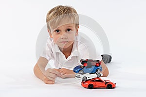 Nice looking very young boy lying with a pile of car toys and having a sincere neutral and proud look in his face