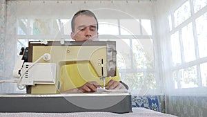 A nice man is sitting at the electric sewing machine at home. He sews several layers of fabric and serves a working tool