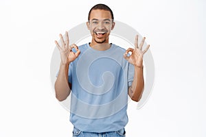 Nice, not bad. Smiling arab man shows okay, ok sign, recommends smth awesome, stands over white background