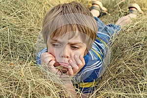 Nice offended kid with insulted expression face, lies on the hay (concept of children\'s emotions)