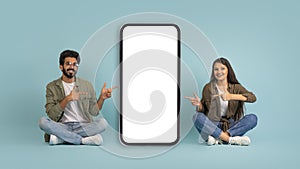 Nice offer. Happy indian couple pointing at big smartphone, mockup