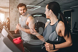 Nice picture of two cheerful people hacving the same workout on the running machine. Besides working they are talking