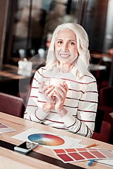 Pleasant senior woman holding a cup of tea and smiling