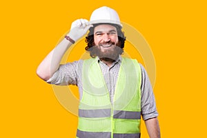 A nice portrait of a young bearded architect smiling at the camera is holding his white helmet near a yellow wall